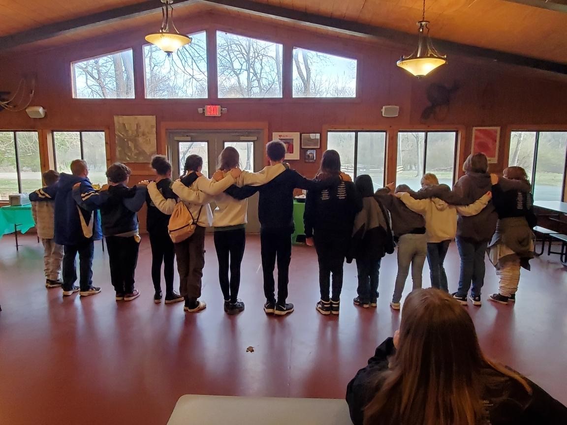 Children stand with interlocking arms on shoulders facing away