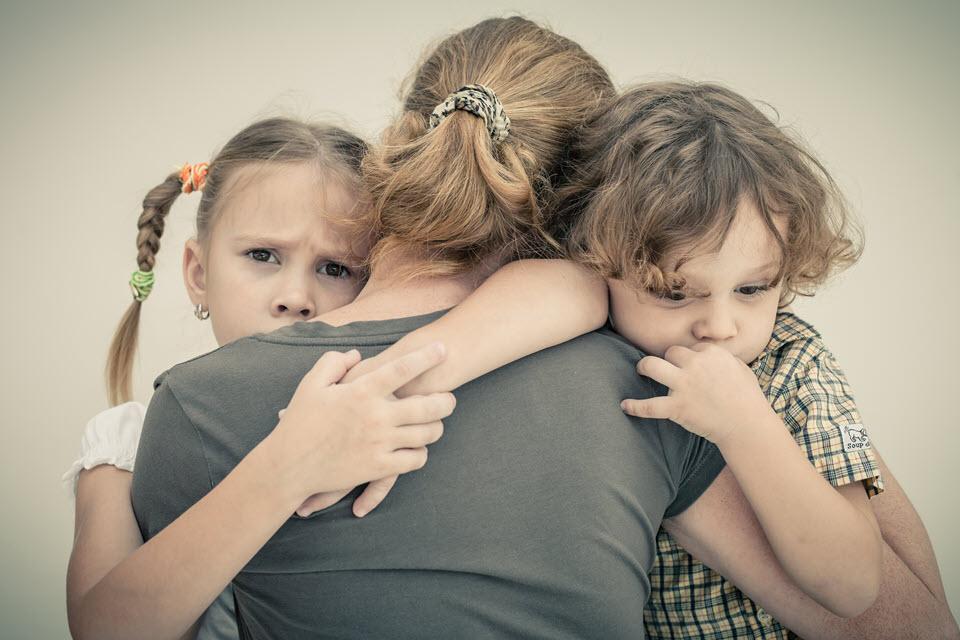 Woman hugs two children with concerned expressions