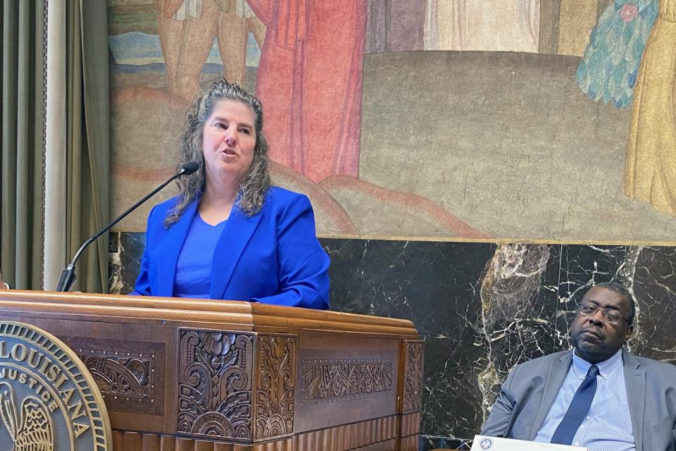 Administrator Liz Ryan standing behind a podium. Seated to her left is SULC Chancellor John Pierre