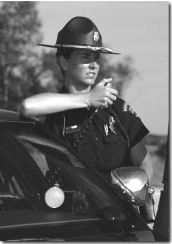 Photograph of police officer standing outside of a patrol car talking on the radio.