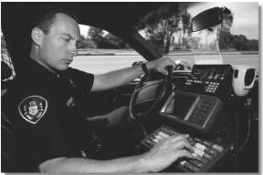 Photograph of police officer sitting in a patrol car working on a computer.